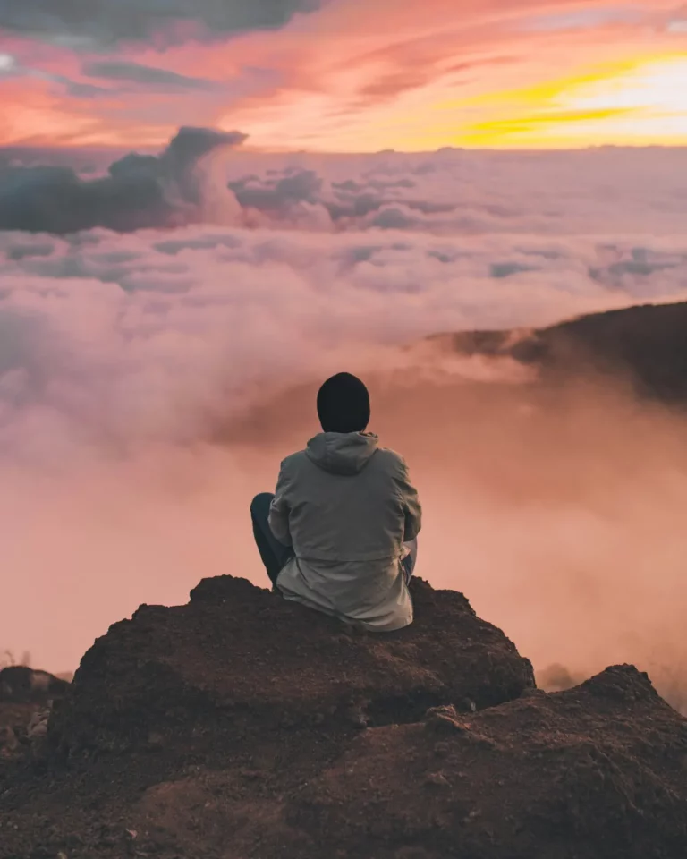 Person sitzt auf einem Felsen über den Wolken